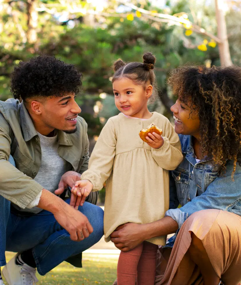 Família sorridente com uma criança pequena em um parque, em momento de afeto ao ar livre